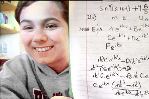 Person holding up hand-written physics notes to a webcam.
