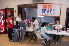 'Cuse Spot cooking class. Children at the table on the left chop vegetables while children on the right measure ingredients for Sloppy Joes