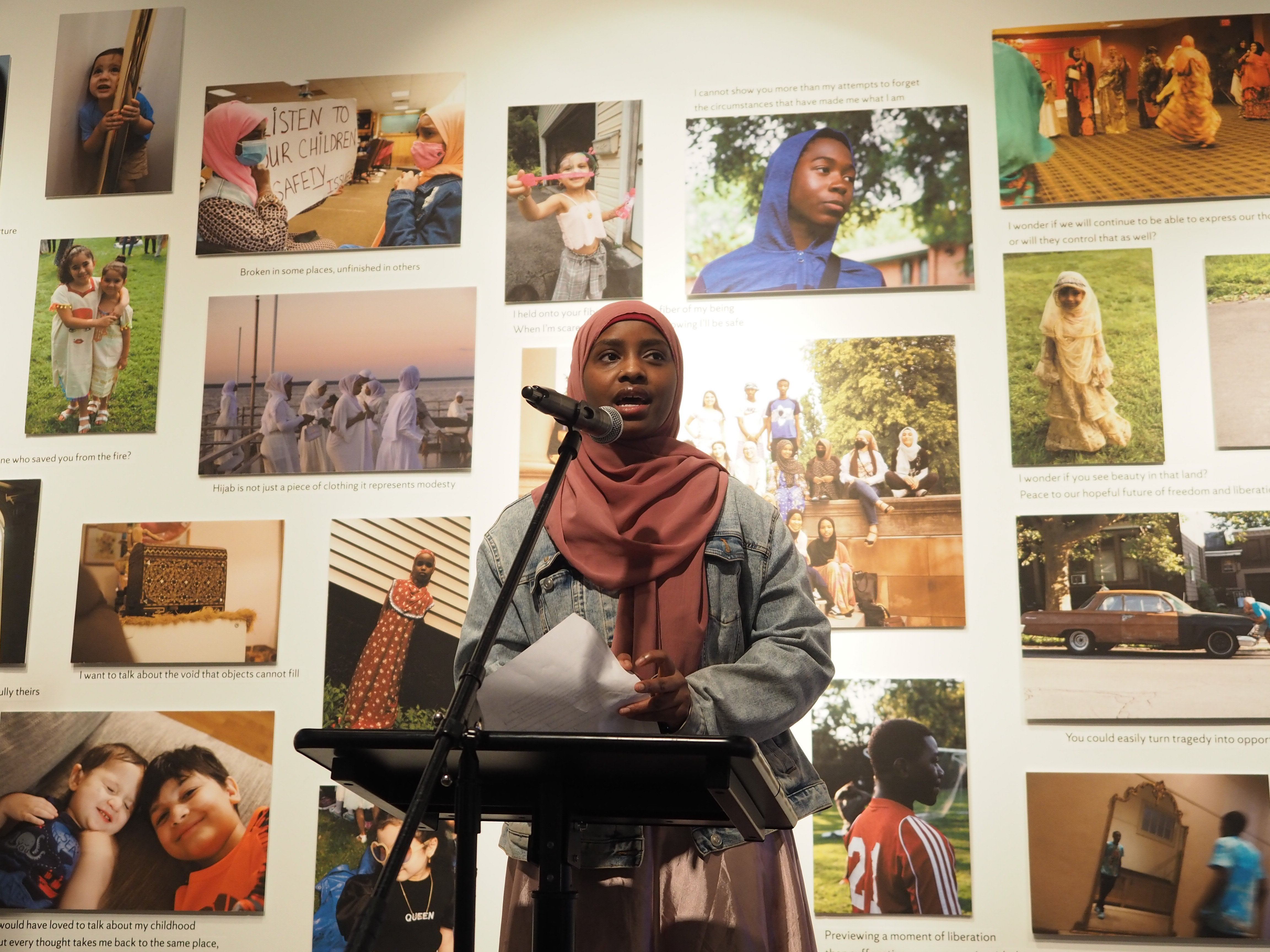 youth woman reads poetry in front of a wall of photographs