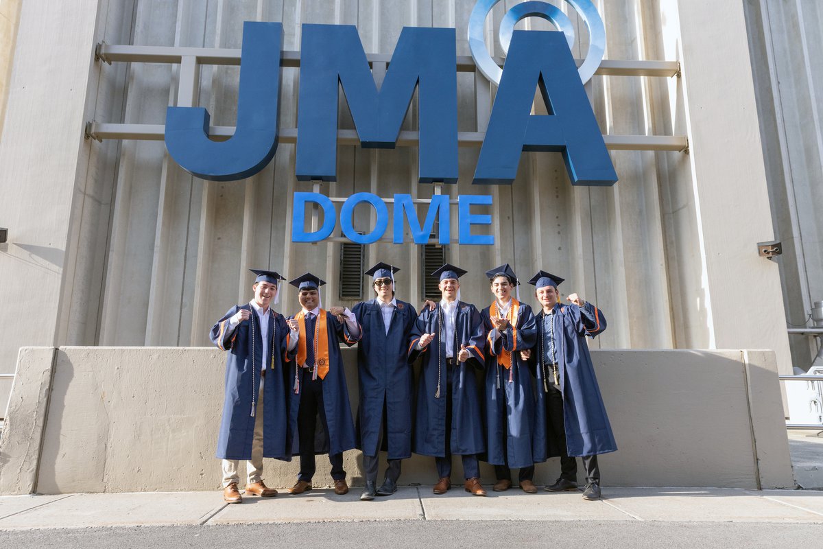 A group of students take a photo underneath the JMA Wireless Dome sign.