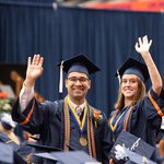 Two graduating students waving and smiling in their cap and gowns.