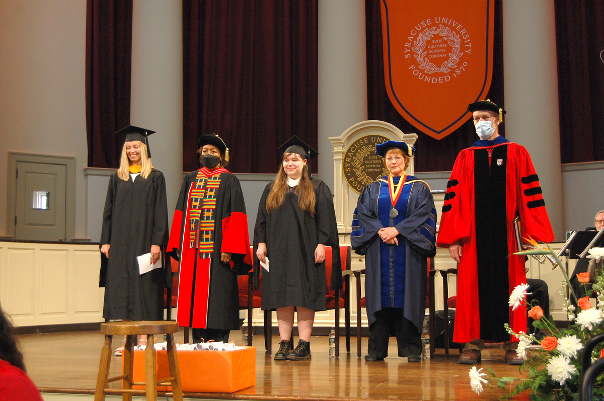 Speakers at the master's convocation stand on stage during ceremony.