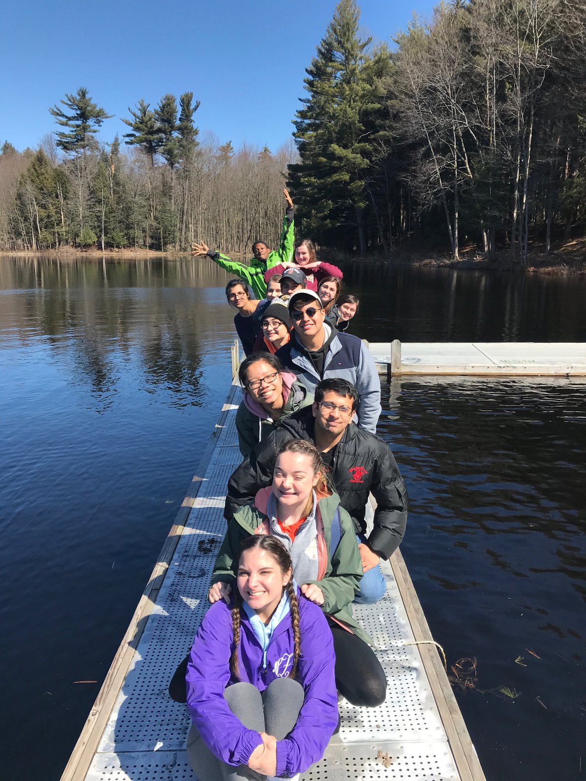 The 2021 SUSTAIN cohort posing on a dock with a lake in the background at Camp Talooli .
