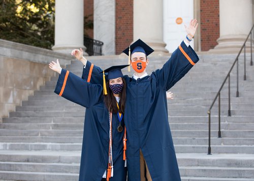 Two students outside of Hendricks Chapel with their caps, gowns and masks