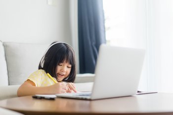 A young girl smiles behind a laptop.