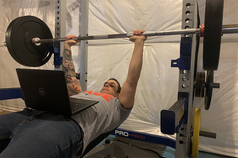 man bench pressing while reading emails on laptop