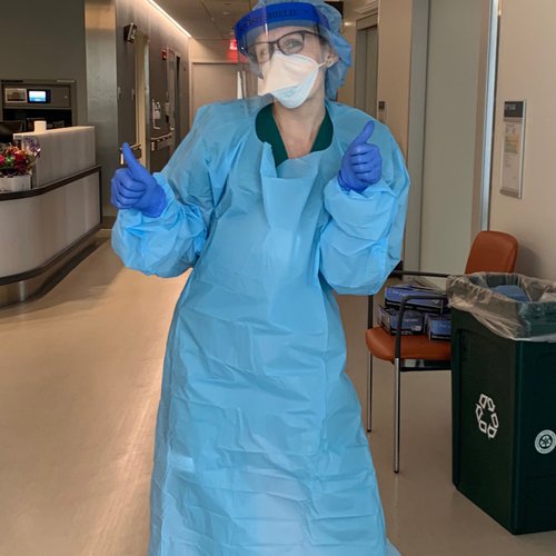 Nurse Meagan Humphrey in scrubs, gloves, and a face mask giving two thumbs up.
